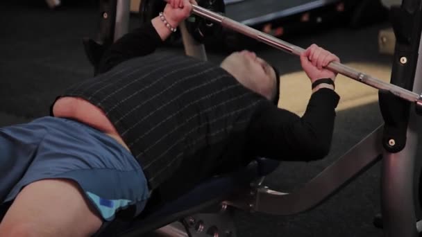 Joyeux homme gras effectue la mauvaise presse banc dans la salle de gym
. - Séquence, vidéo