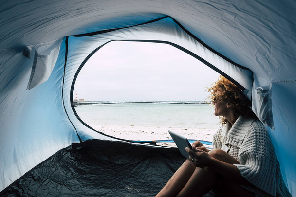 Traveler lifestyle concept with young beautiful woman inside a ten camping on the beach with ocean and lighthouse view for summer vacation day - outdoor free camp - 写真・画像