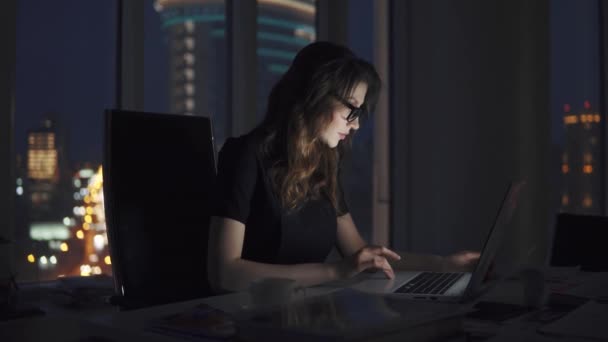 fiatal üzleti nő dolgozik későn az irodában. az éjszakai város hátterére szemüveges lány portréja - Felvétel, videó