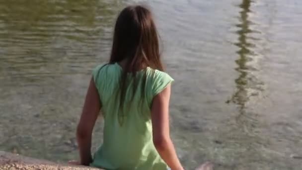 beautiful young girl sitting near river - Materiał filmowy, wideo