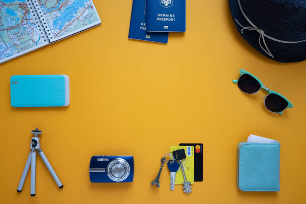 auf gelbem Hintergrund Dinge zum Reisen: blaue Pässe, Karte, Geldbörse mit Geld, Schlüssel, Kreditkarte, Hut, Sonnenbrille, Powerbank, Fotokamera und Stativ, Blick von oben - Foto, Bild