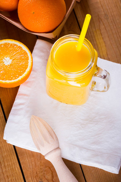 Orange fruits and juice on white napkin. Citrus fruit for making juice with manual juicer. Oranges in wooden box on wooden boards. Mason jar with orange juice - Фото, изображение