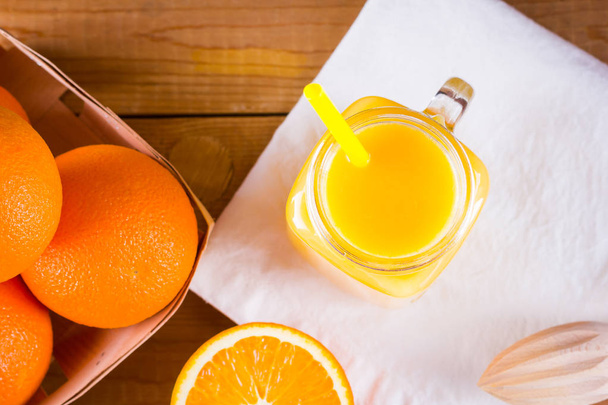 Orange fruits and juice on white napkin. Citrus fruit for making juice with manual juicer. Oranges in wooden box on wooden boards. Mason jar with orange juice - Foto, Imagem