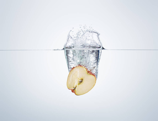apple slice falls into the water scattering a lot of splashes an - Fotó, kép