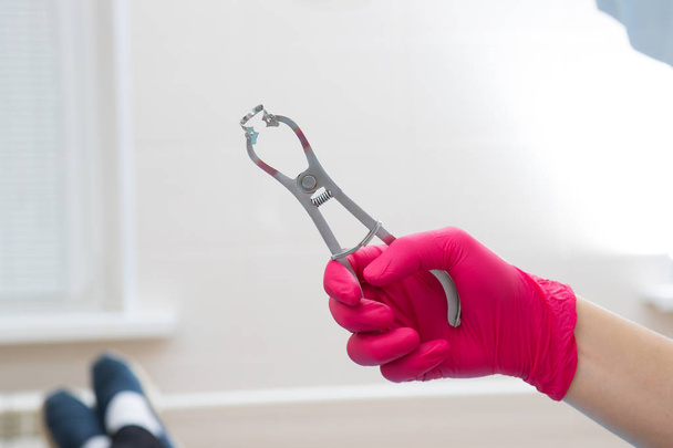 Close up of dentist hand in red medical glove. In his hand, a tool for installing an insulating wipe in the patient's mouth - Fotografie, Obrázek