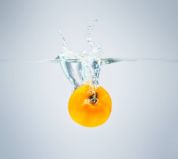 yellow tomato falls into the water scattering a lot of sprays an - Photo, Image