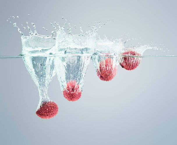 Lychee berries fall into the water scattering a lot of splashes  - Photo, Image