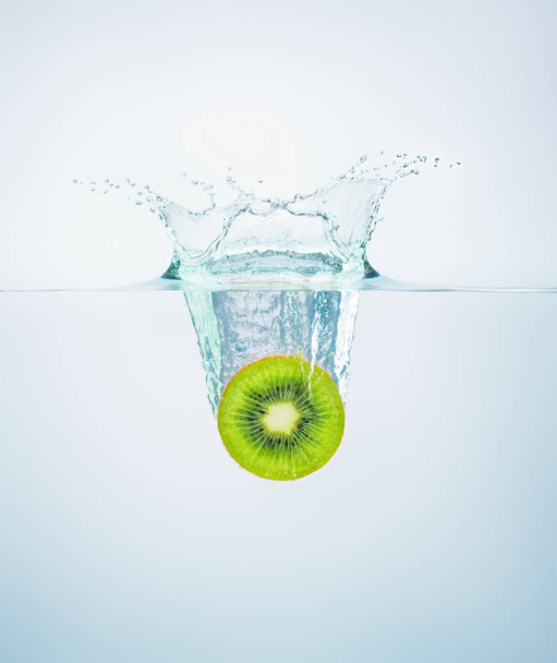 slice of kiwi falls into the water scattering a lot of splashes  - Foto, immagini