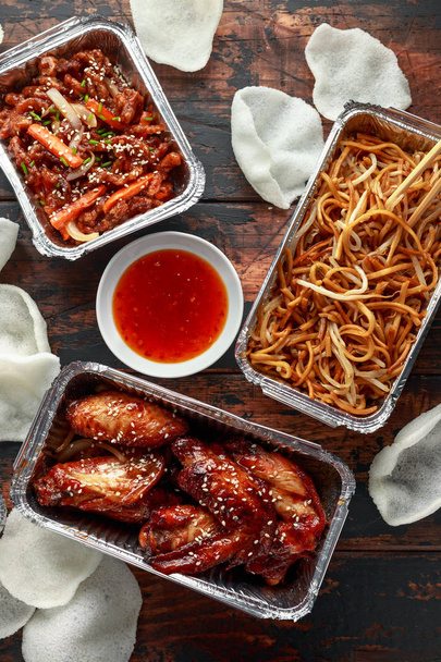 Chinese takeaway food. Crispy shredded beef, sweet and sour chicken wings, egg noodles with bean sprouts, pineapple, chilli dip and prawn crackers - Photo, Image