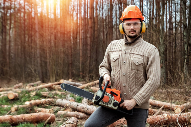 Logging, Worker in a protective suit with a chainsaw. Cutting down trees, forest destruction. The concept of industrial destruction of trees, causing harm to the environment. - Photo, Image