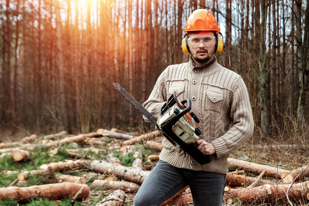Logging, Worker in a protective suit with a chainsaw. Cutting down trees, forest destruction. The concept of industrial destruction of trees, causing harm to the environment. - Foto, afbeelding