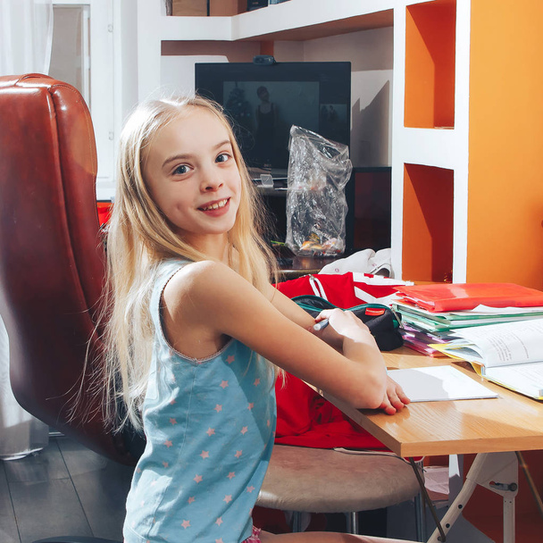 Beautiful little blonde girl sits at the table and does homework - Photo, Image