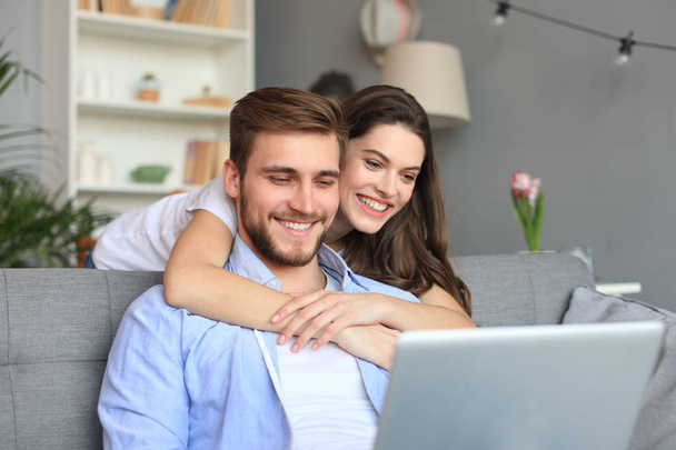Young couple doing some online shopping at home, using a laptop on the sofa. - Foto, Bild