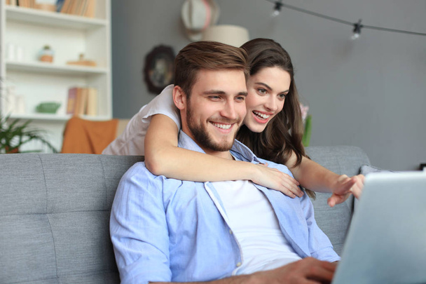Young couple doing some online shopping at home, using a laptop on the sofa. - Foto, Imagen