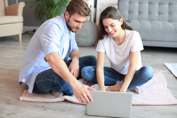 Young couple doing some online shopping at home, using a laptop on floor. - Фото, изображение
