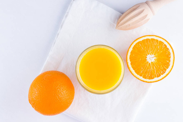 Orange fruits with juice, concept. Orange juice and halves of oranges on white background. Citrus for making juice and manual juicer. Whole and squeezed oranges and glass of juice - Photo, Image