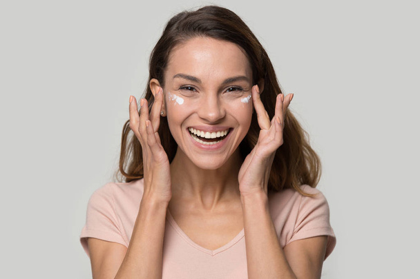 Happy woman looking at camera applying eyelid moisturizing cream - Foto, Imagen