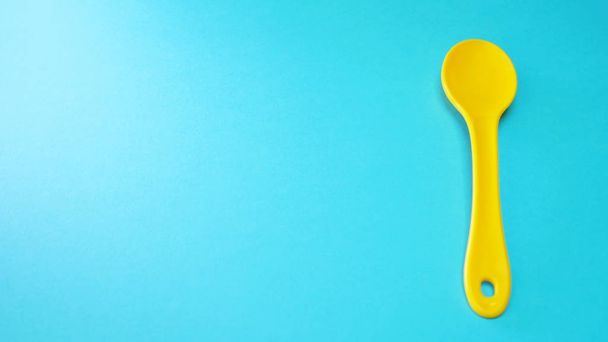 Yellow plastic spoon at blue background isolated - Фото, изображение