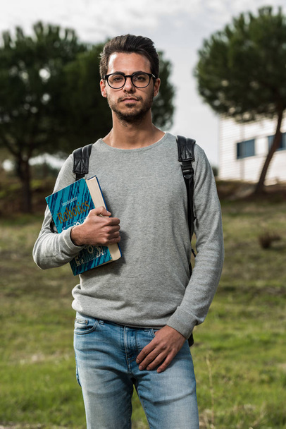 Young student of computer science poses with a robotics book next to one of the buildings of the Polytechnic School - Photo, Image
