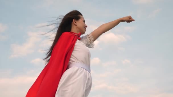 schöne Superheldenmädchen steht auf einem Feld in einem roten Mantel, Mantel flattert im Wind. Mädchen träumt davon, ein Superheld zu werden. Zeitlupe. junge Frau spielt in rotem Mantel mit Ausdruck von Träumen. - Filmmaterial, Video