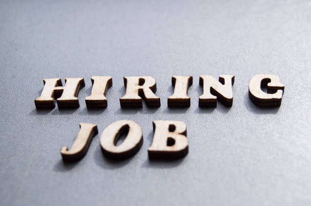 O conceito de contratação de trabalhadores, escrito por HIRING JOB em letras de madeira em um fundo cinza com foco seletivo e espaço para o seu - Foto, Imagem