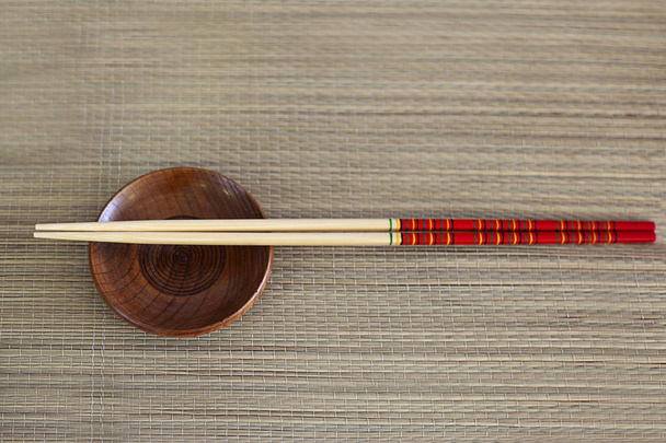 Two wooden chopsticks, small brown bowl served on wooden background. Asian traditional bamboo appliances for eating.  Sushi Set. Blank space  - Фото, зображення