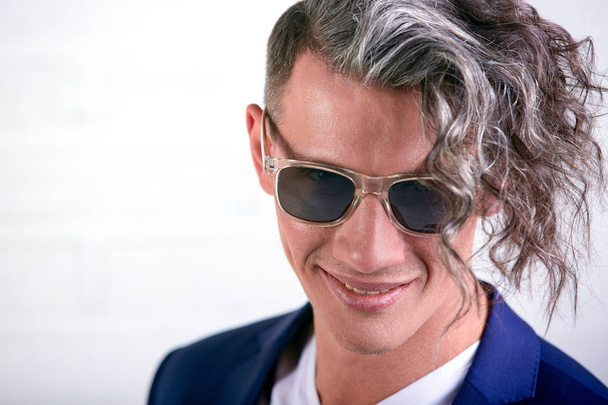 Retrato de un hombre de negocios elegante con el pelo largo rizado en gafas de sol sonriendo a la cámara sobre fondo blanco
 - Foto, imagen