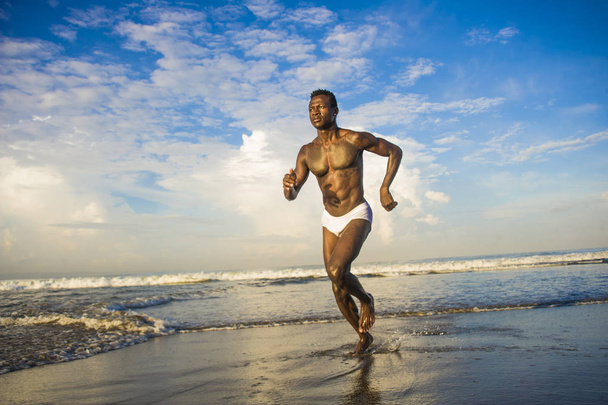 幸せで魅力的な黒アフロアメリカンマンフィット健康で、筋肉の体がビーチの海の水の上で実行している楽しい夏の休日を楽しむ楽しみを持つ - 写真・画像