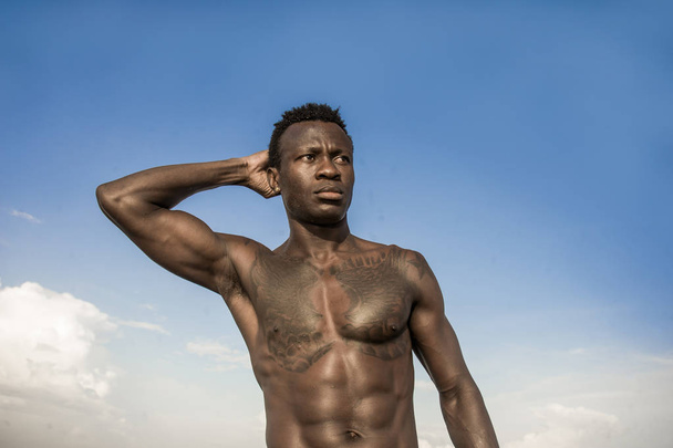 portrait of young attractive and fit black African American man with strong muscular body posing cool model attitude on the beach isolated on Summer blue sky - Foto, afbeelding