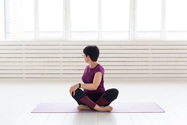 Emberek, jóga, sport és egészségügyi koncepció - a vonzó középkorú nő, nyúlik, és ül a jóga lótusz helyzet - Fotó, kép