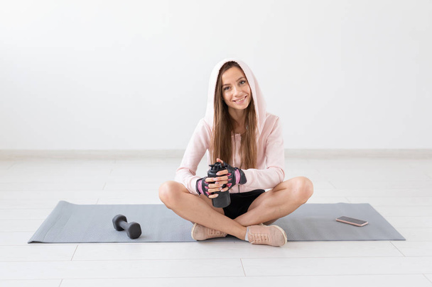 Healthy lifestyle, people and sport concept - Woman sitting on yoga mat and drinking water after hard workout - 写真・画像