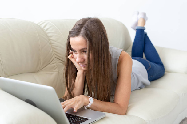 Технологии, фрилансер и концепция людей - красивая молодая женщина лежит на диване с ноутбуком
 - Фото, изображение