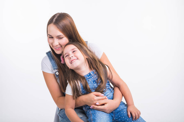 Elternschaft, Familien- und Kinderkonzept - Porträt einer Mutter und ihres kleinen Mädchens haben Spaß und lächeln vor weißem Hintergrund - Foto, Bild
