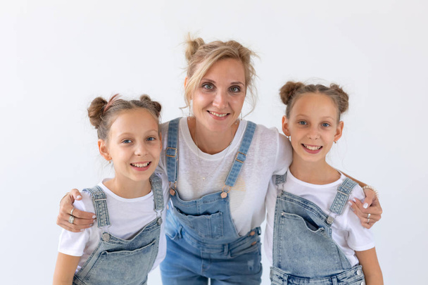 Familie, zussen en liefde concept - moeder knuffelen twee tweelingdochters op witte achtergrond - Foto, afbeelding