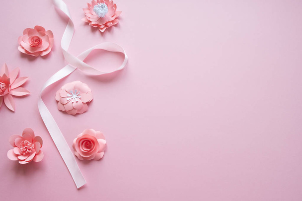 frame with pink paper flowers and pink ribbon on pink background. - Photo, Image