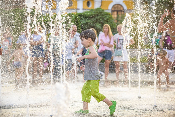 Aufgeregter Junge, der sich zwischen Wasserstrahlen im Springbrunnen vergnügt. Sommer i - Foto, Bild