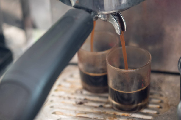 Κοντινό πλάνο του εσπρέσο που χύνεται από τη μηχανή του καφέ μέχρι το γυαλί. Επαγγελματική Παρασκευή καφέ - Φωτογραφία, εικόνα