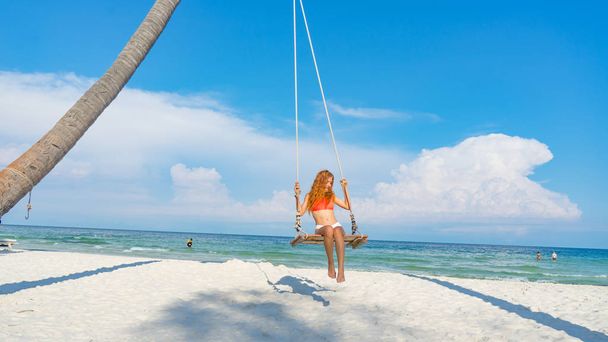 Red haired girl in bikini swinging on the beautifyl beach with white sand and crystal water in Phu quoc island Vietnam ,travel concept - 写真・画像