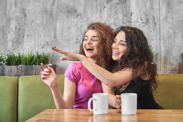 Giovani ragazze sedute in caffè e pettegolezzi mentre bevono tè
 - Foto, immagini