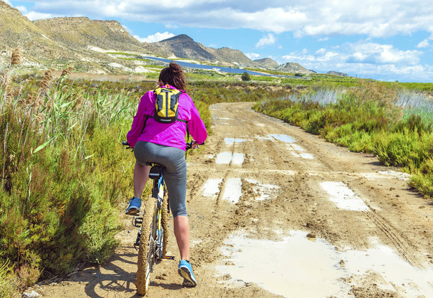 Woman riding a mountain bike by a muddy path of dirt. - Photo, Image