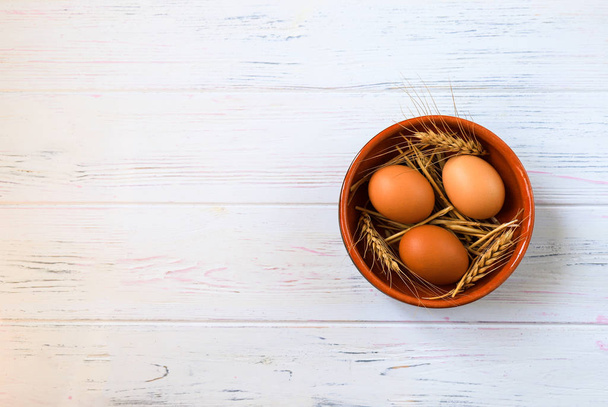 Hnědá organická kuřecí vejce v keramickém kulatém plechu s pšeničným uchem na světle dřevěné pozadí, Velikonoční koncept. Jaro, letní jídlo - Fotografie, Obrázek
