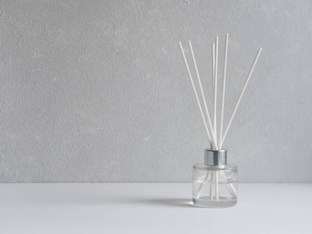 Aromatizer. Aromatic air freshener in a transparent glass bottle with white reeds on a gray background - Foto, Bild