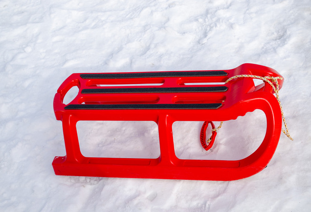 trineo rojo de plástico con patio de borde negro en invierno
 - Foto, Imagen