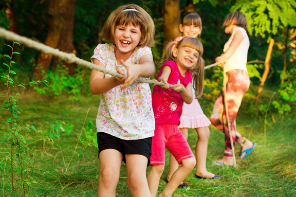 Skupina šťastných dětí hraje přetahovanou venku na trávě. Děti tahání lana v parku. - Fotografie, Obrázek