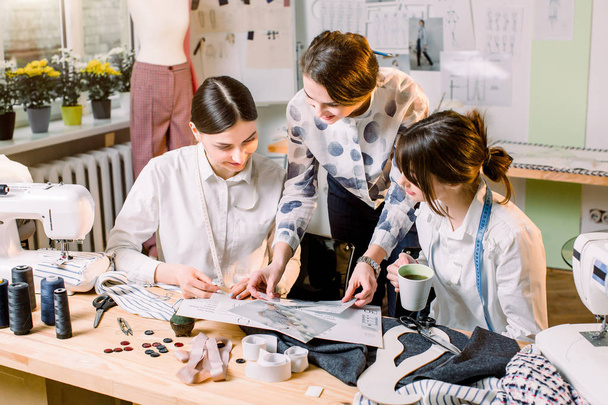 Three attractive young fashion designers carefully creating new fashionable styles of pants. Dressmakers making clothes. Fashion, dressmaker, sewing concept - Foto, Imagem