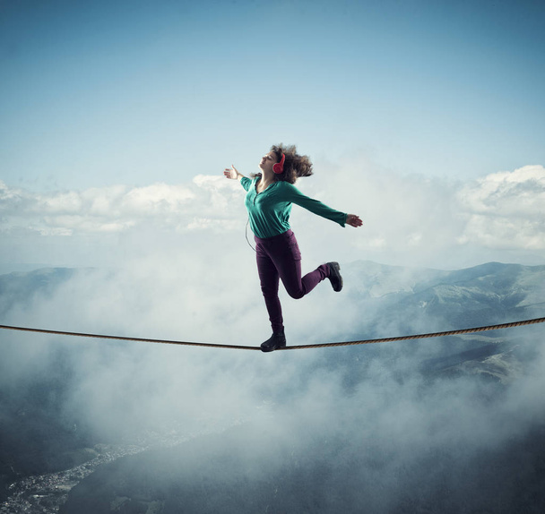 Жінка балансує на мотузці над хмарами та горами, слухаючи музику. Концепція свободи
. - Фото, зображення