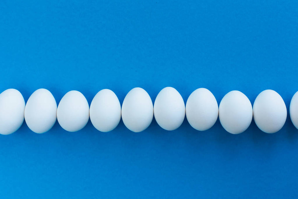 White chicken eggs on a blue background lined with a line. Healthy organic food and diet concept. Easter theme - Foto, Imagen