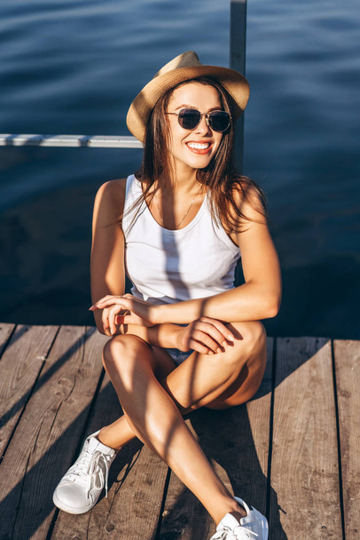 Cute young brunette girl relaxing on the pier near lake. - Valokuva, kuva