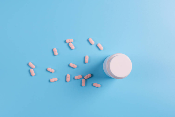 Rózsaszín tabletta tabletta és a kék alapon fehér üveg.  - Fotó, kép