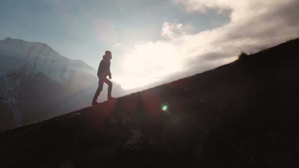 Vista aérea de tiro épico de un hombre caminando en el borde de la montaña como una silueta en una hermosa puesta de sol. Silueta de un hombre con barba y sombrero trepando cuesta arriba
 - Metraje, vídeo